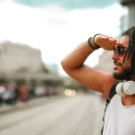 Stylish young man with sunglasses and headphones, enjoying a sunny day outdoors in the city.